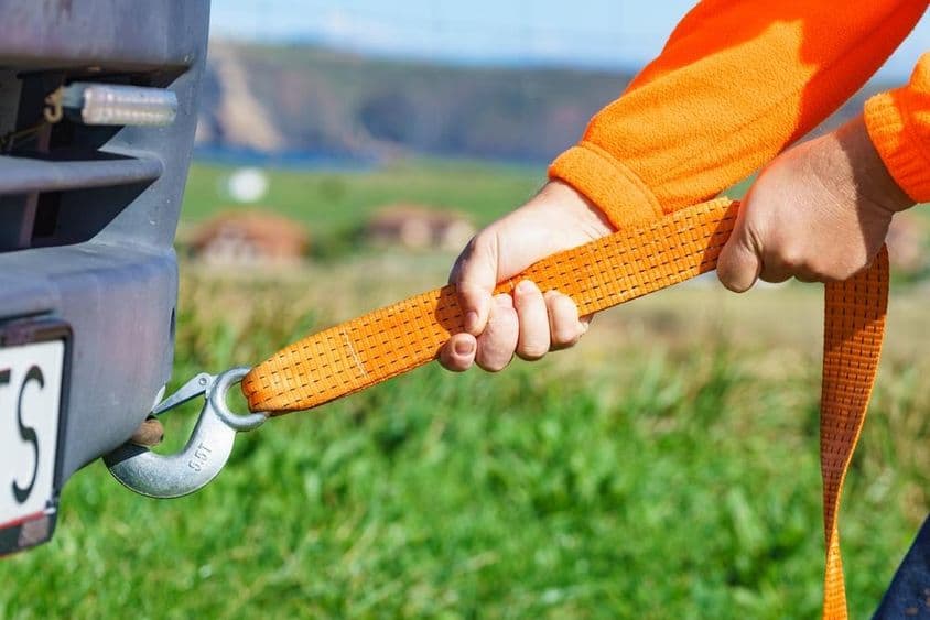 A férfi kéz a vonókötél hevederét a vontatószemhez akasztja.