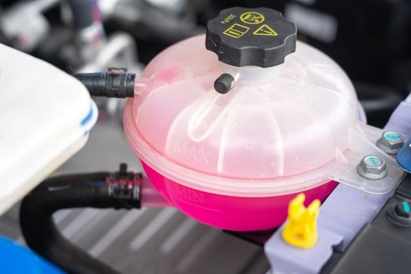 Egy autó motorjának hűtőfolyadék-ellátó tartálya rózsaszín fagyálló folyadékkal töltve.