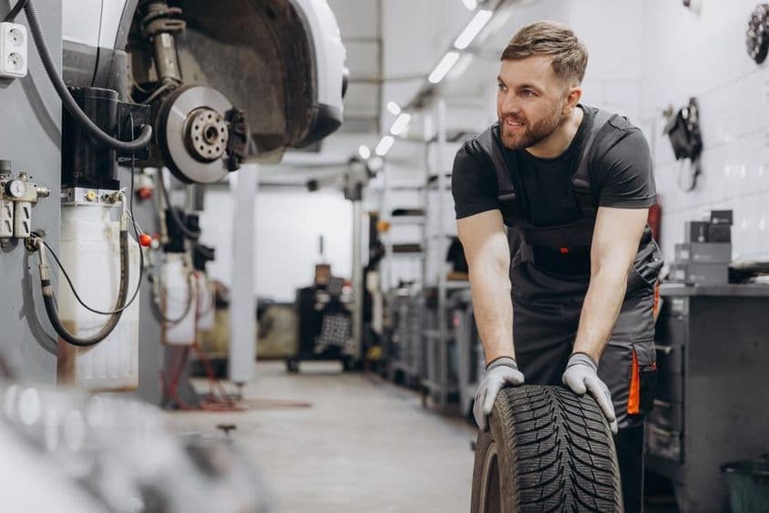 Autószerelő dolgozik a garázsban és cseréli a kereket.