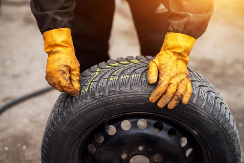 Narancssárga kesztyűs szerelő krétával jelöli a gumiabroncsokat.