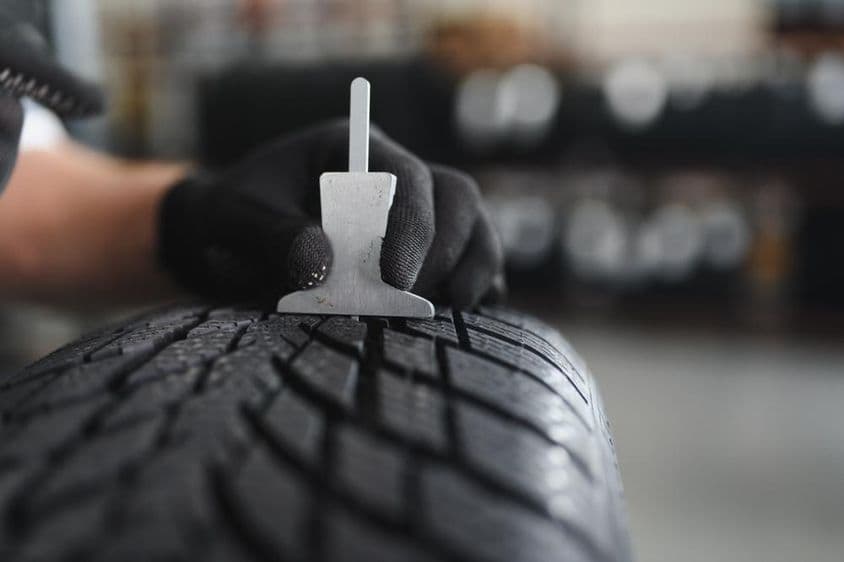 Egy autószervizben dolgozó munkás egy speciális szerszámmal megméri a profil mélységét.