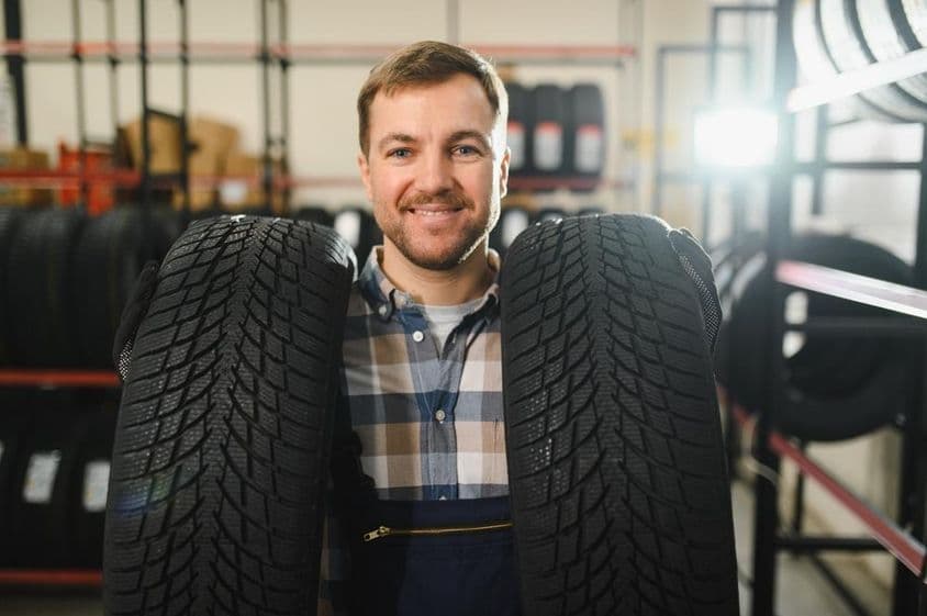 férfi szerelő új gumiabroncsot tart a kezében.