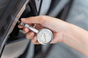 Egy személy egy autó gumiabroncsnyomását ellenőrzi.