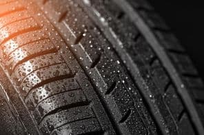 Autó nyári gumiabroncsának futófelület-mintázatának közeli képe vízcseppekkel.