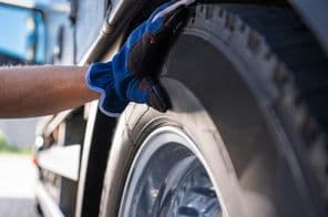 Egy kesztyűs szerelő ellenőrzi a teherautó gumiabroncsainak állapotát.