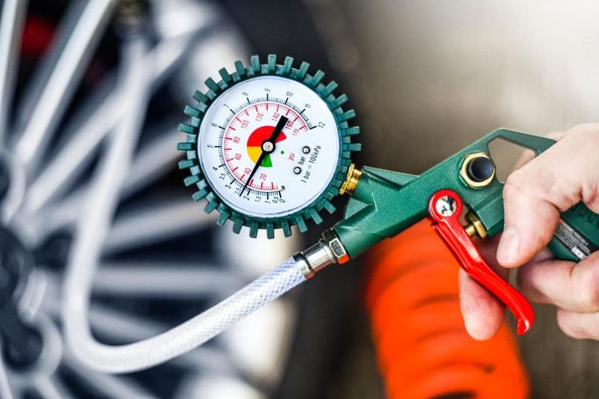 Autószerelő felfújja a gumiabroncsot és ellenőrzi a légnyomást.