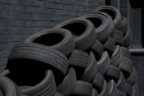 Használt fekete autógumik hevernek rendezetlenül egy fekete falnak támaszkodva.
