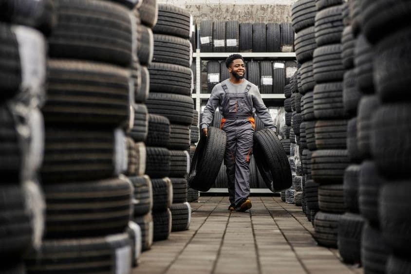 Mosolygó autószerelő cipel autógumikat egy autószervizben.