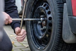 Egy autószerelő kezében egy villáskulcs épp csavarja be az autó kerékcsavarjait.