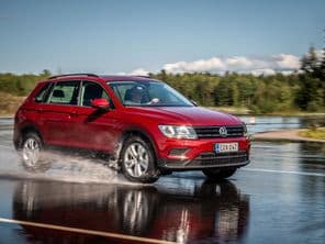 Piros Volkswagen Tiguan halad csúszós, nedves úton egy tesztpályán.
