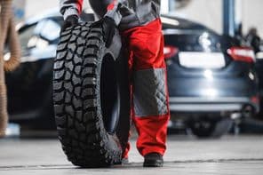 Férfi szerelő és új nagy gumiabroncs off road autós javító műhelybe.