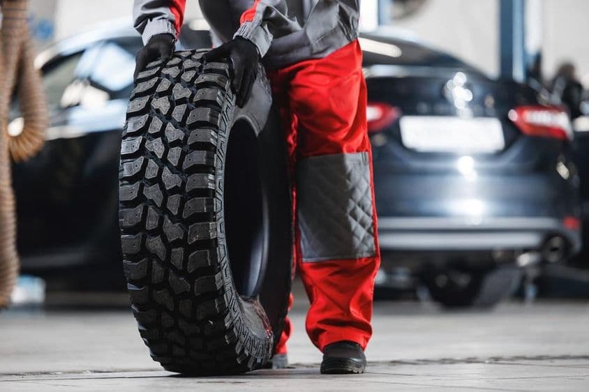 Férfi szerelő és új nagy gumiabroncs off road autós javító műhelybe.