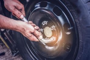 Autógumi csere, kéz a villáskulcson csavarok rögzítése.