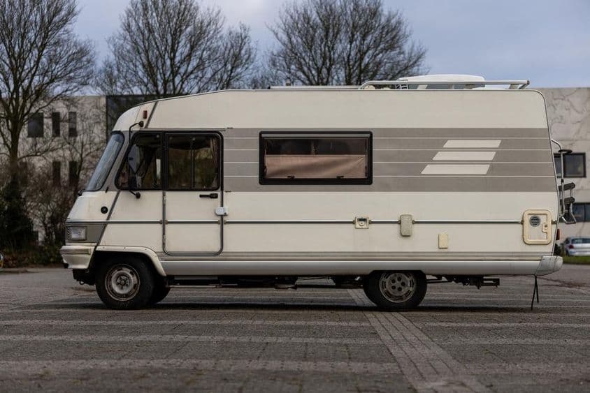 Egy klasszikus bézs színű lakóautó parkolt egy parkolóban.