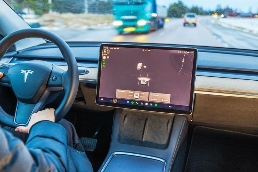 Egy nő Tesla Model Y-t vezet téli úton.