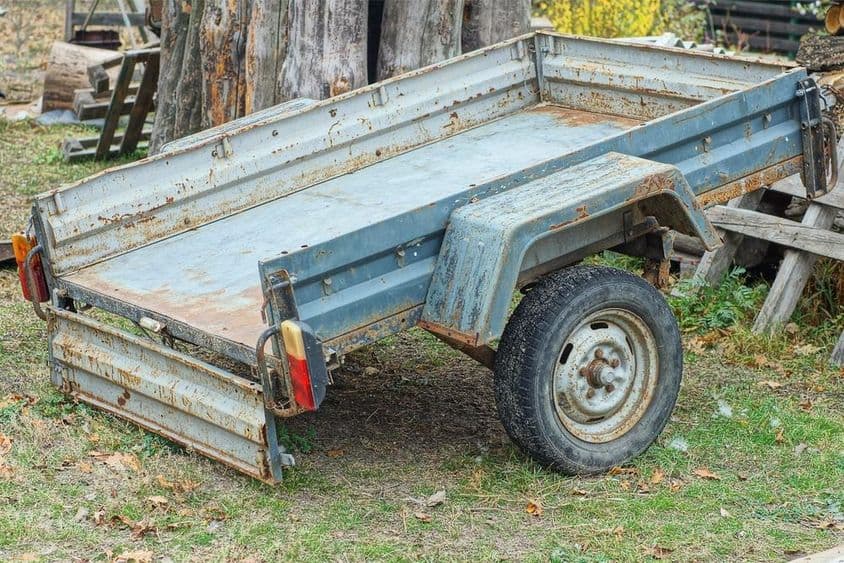 Autó utánfutó áll a földön a vágott fatörzsek közelében.