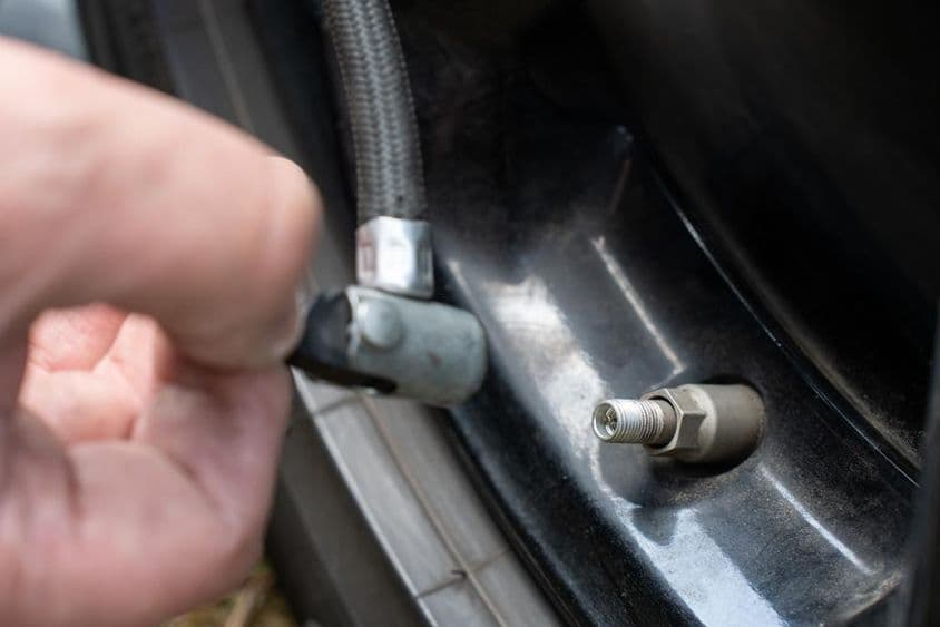 Kezek láthatók, amint egy kompresszortömlőt csatlakoztatnak egy autó szelepéhez.