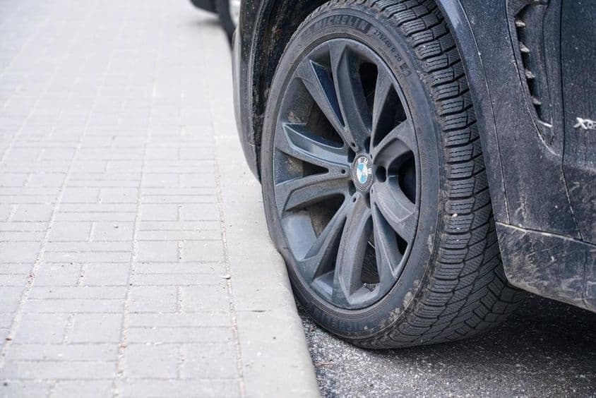 BMW autó kereke parkolt a parkolóban a járdaszegélyhez közel.