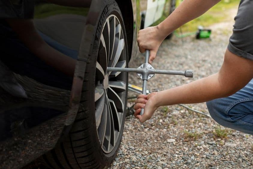 Férfi sofőr kerék kulccsal meghúzza az autója kerekének csavarjait.