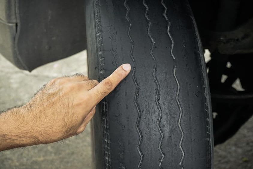 Közeli kép egy férfi kezéről, amint a használattól kopott és kopott gumiabroncsokra mutat.