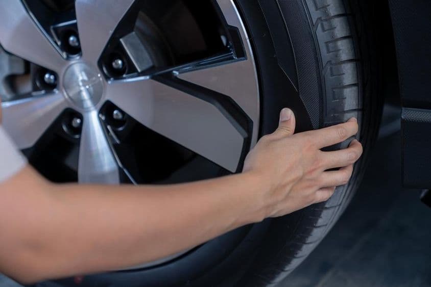 Egy fiatal nő ellenőrzi az autó gumiabroncsainak nyomását.