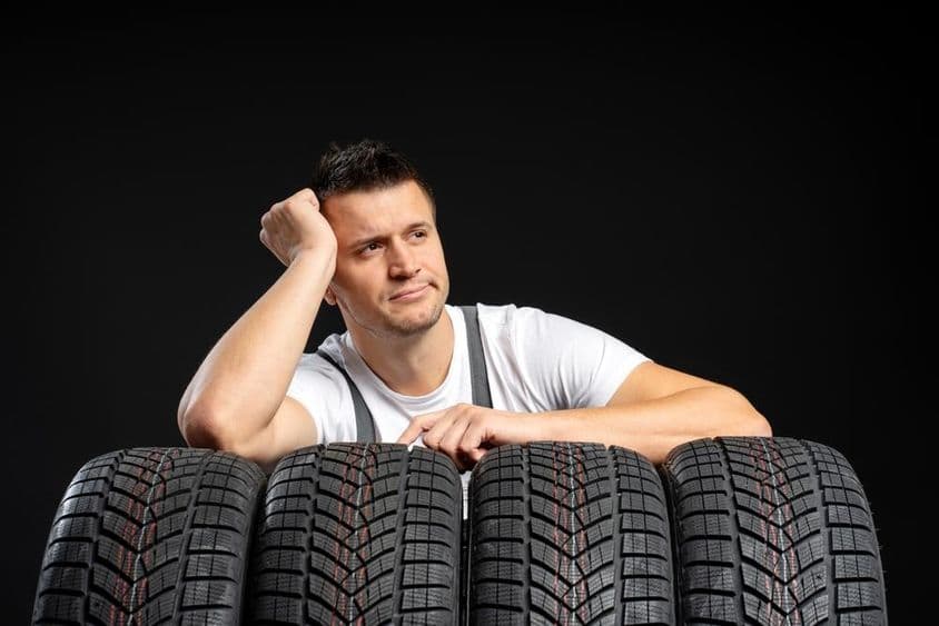 Egy szerelő autógumikra támaszkodik, egy garázsban.