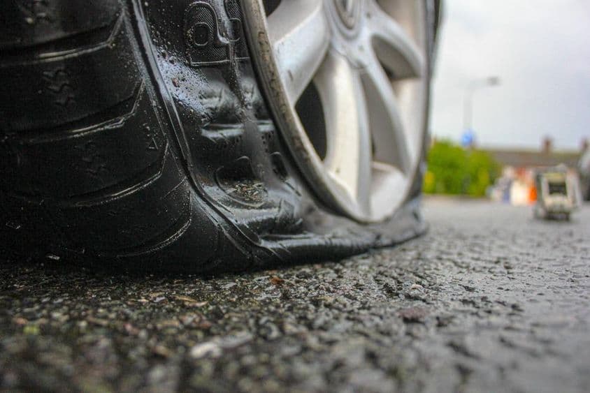 Egy lyukas gumival rendelkező autó útmenti segítségnyújtásra vár.