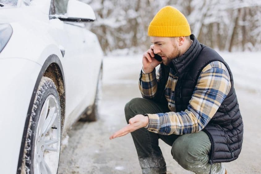 Ember beszél az okostelefonján defektes kocsi mellett