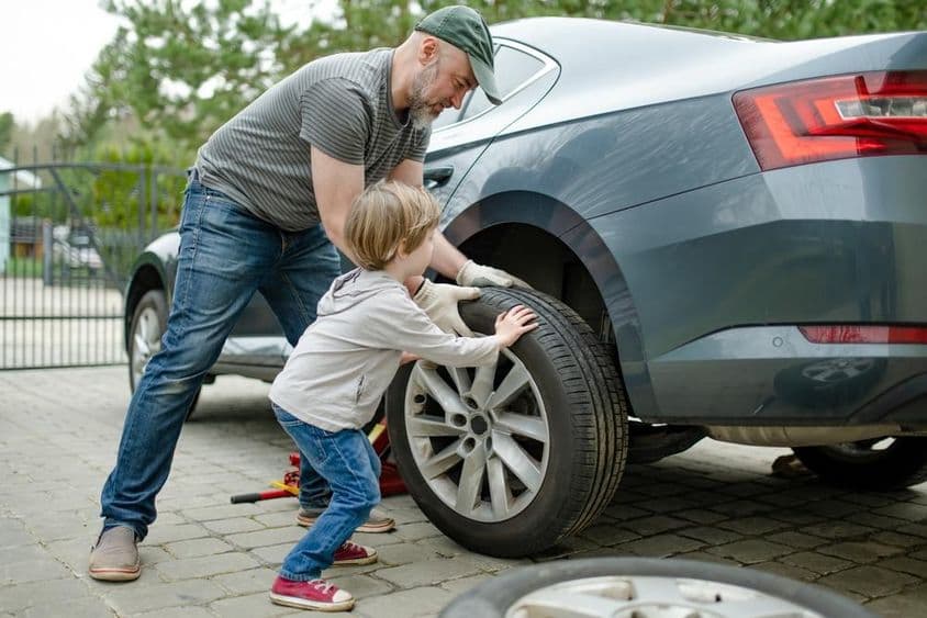Aranyos kisfiú segít az apjának, hogy cseréljen autó kerekét.
