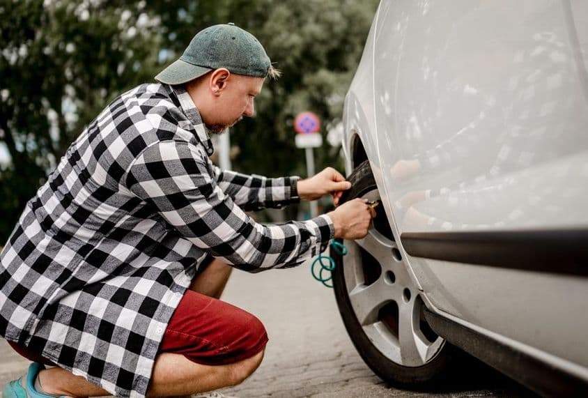 egy férfi az autó szelepéhez csatlakoztatja a légpumpát.